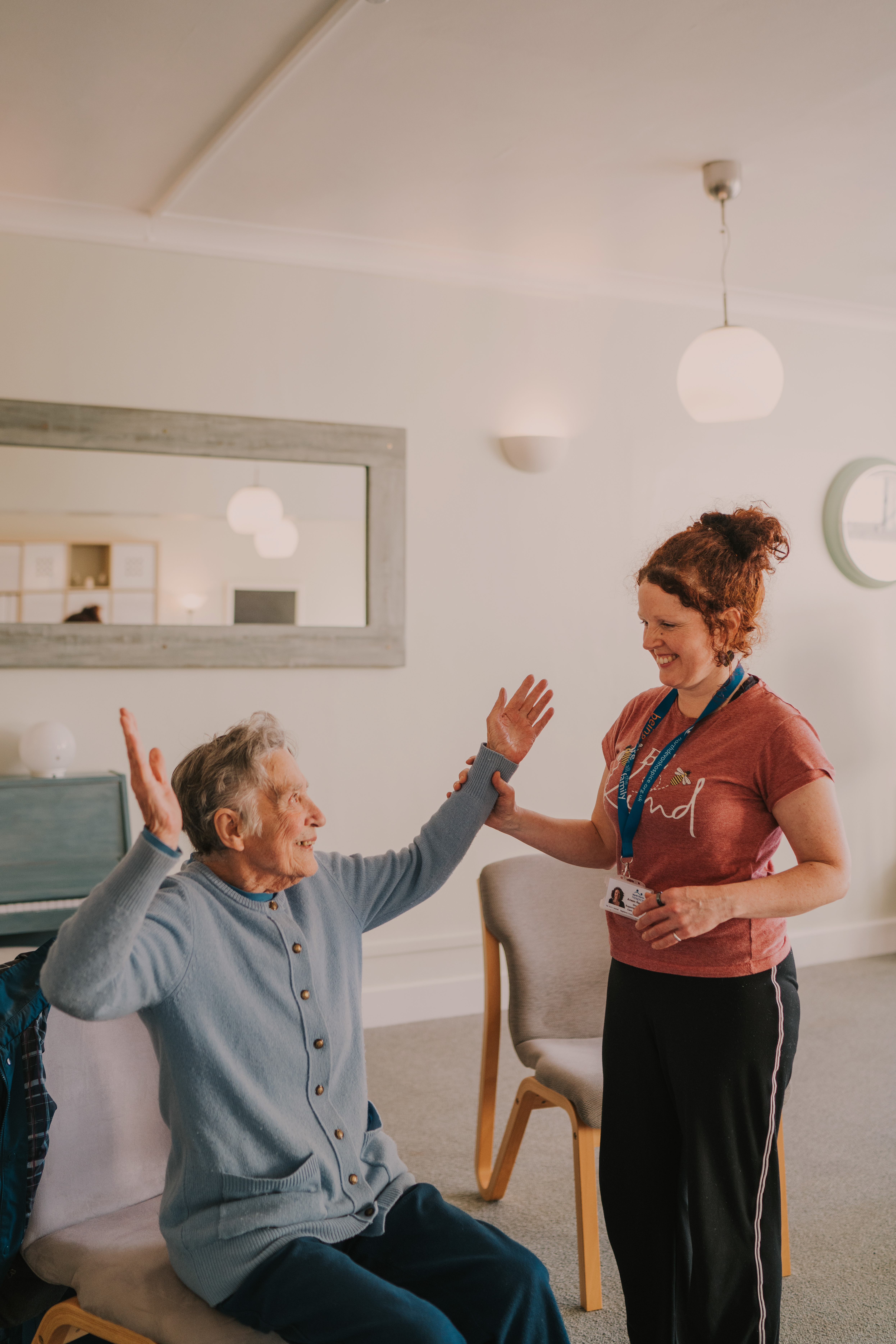 Female yoga instructor stood next to a female patient supporting her arms into a seated yoga pose