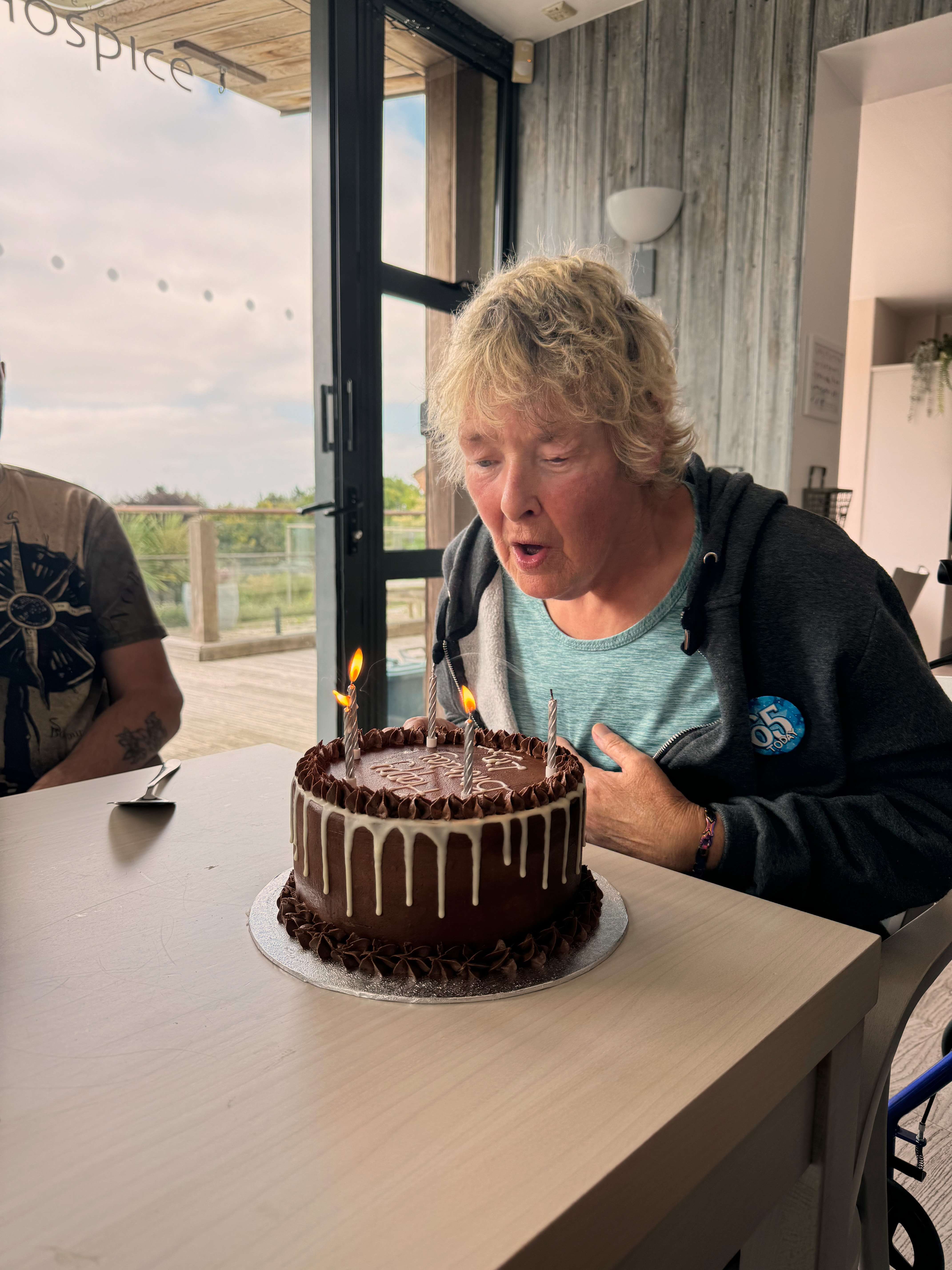 Female patient blowing out candles on a large chocolate birthday cake for a 65th birthday