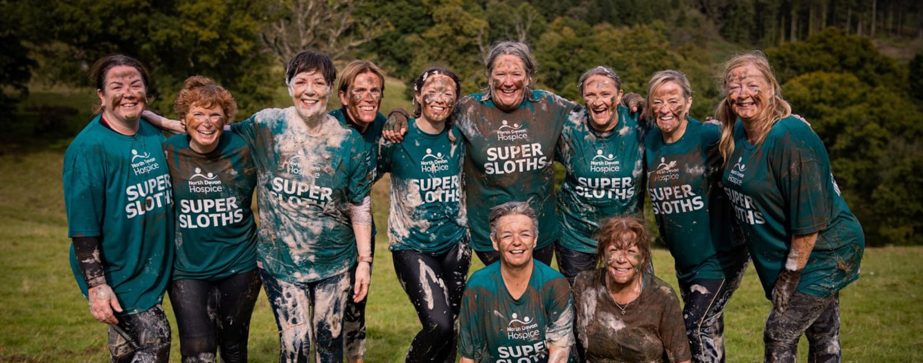 Team of females covered in mud and bubbles, having completed a commando course challenge, smiling to camera
