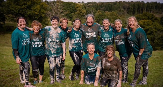 Team of females covered in mud and bubbles, having completed a commando course challenge, smiling to camera