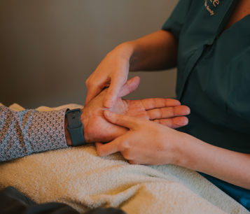 Female complementary therapist performing a hand massage on an elderly male patient with a cream towel underneath