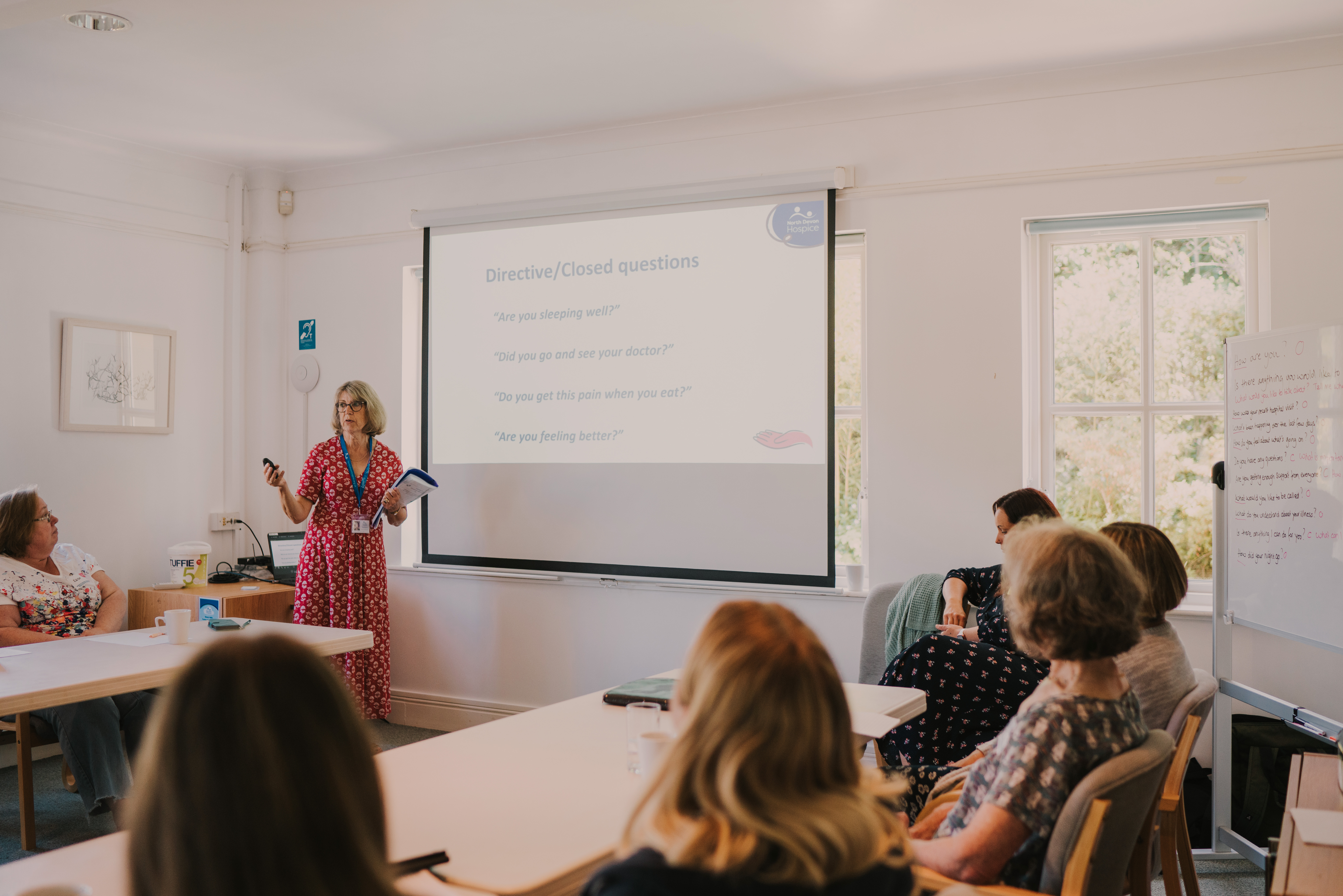 Room of delegates with one female standing at the front, presenting from a projector
