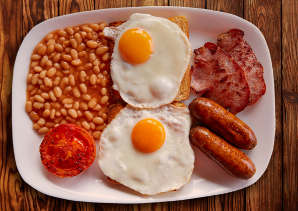 Birds eye view of a full English breakfast on a large white oval plate, sat on a wooden table