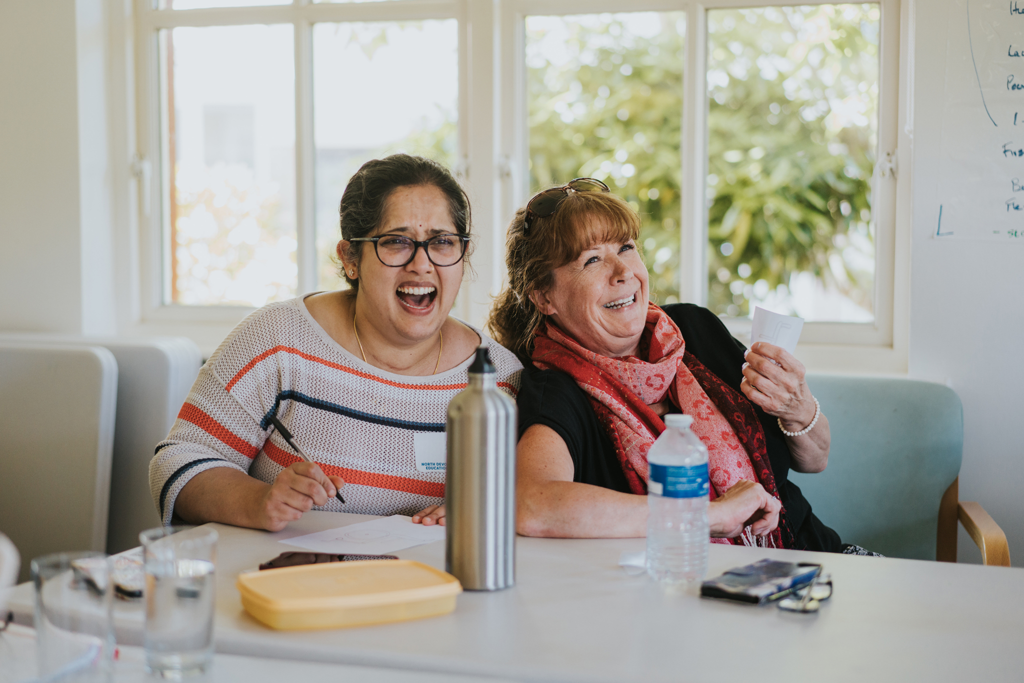 Two female delegates, sat at a table. laughing during a training session