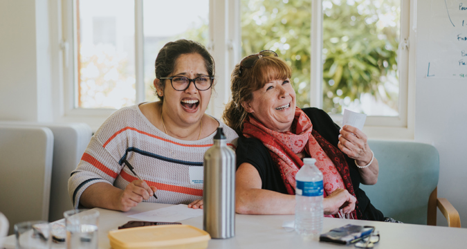 Two female delegates, sat at a table. laughing during a training session