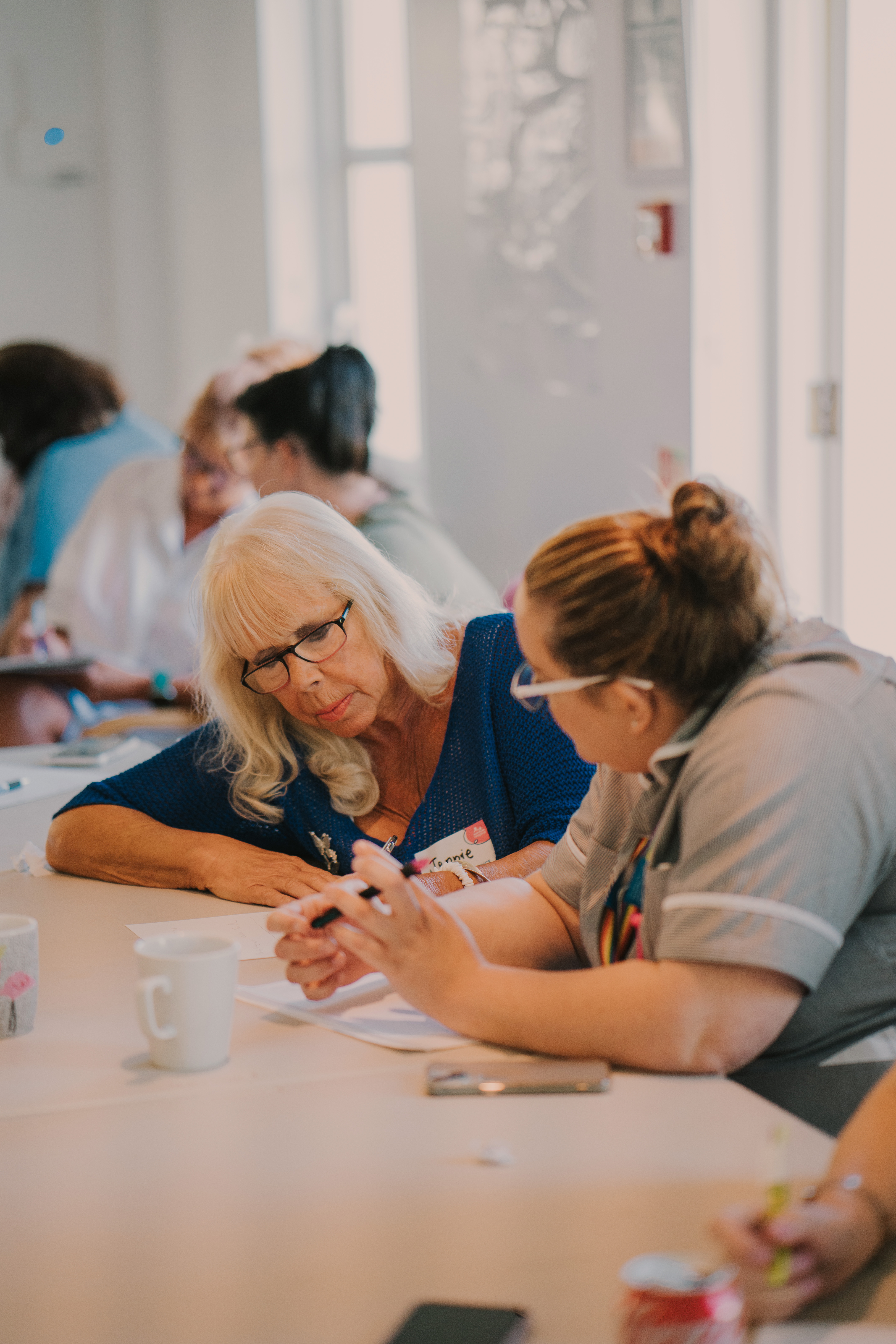 Two female delegates, sat at a table discussing a training manual