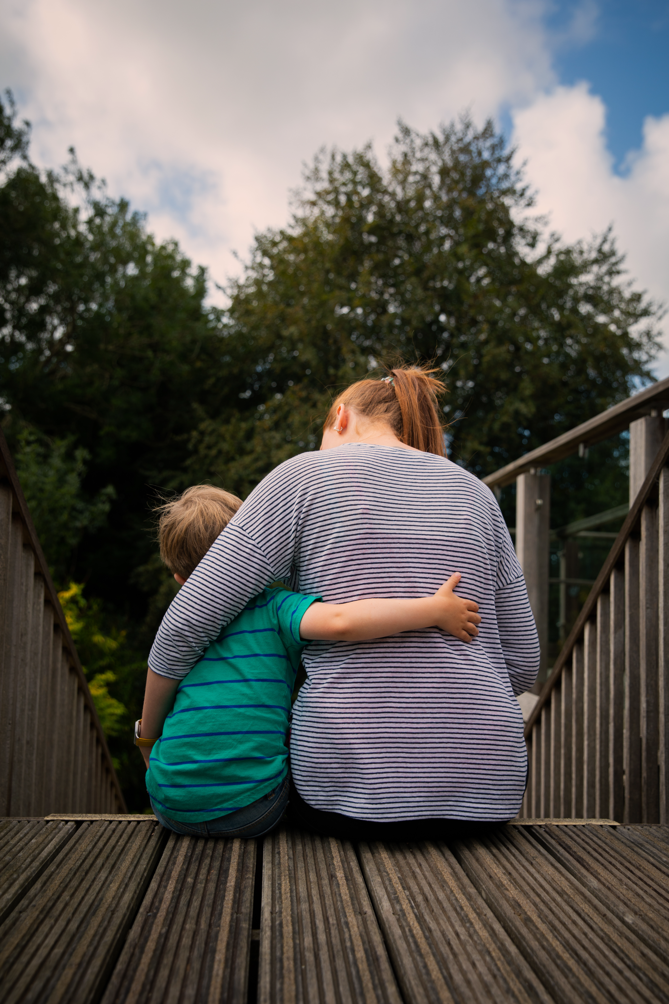 Image from behind a female with striped jumper sat at the top of steps hugging a small boy with green and blue striped t-shirt