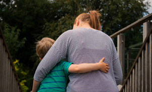 Image from behind a female with striped jumper sat at the top of steps hugging a small boy with green and blue striped t-shirt