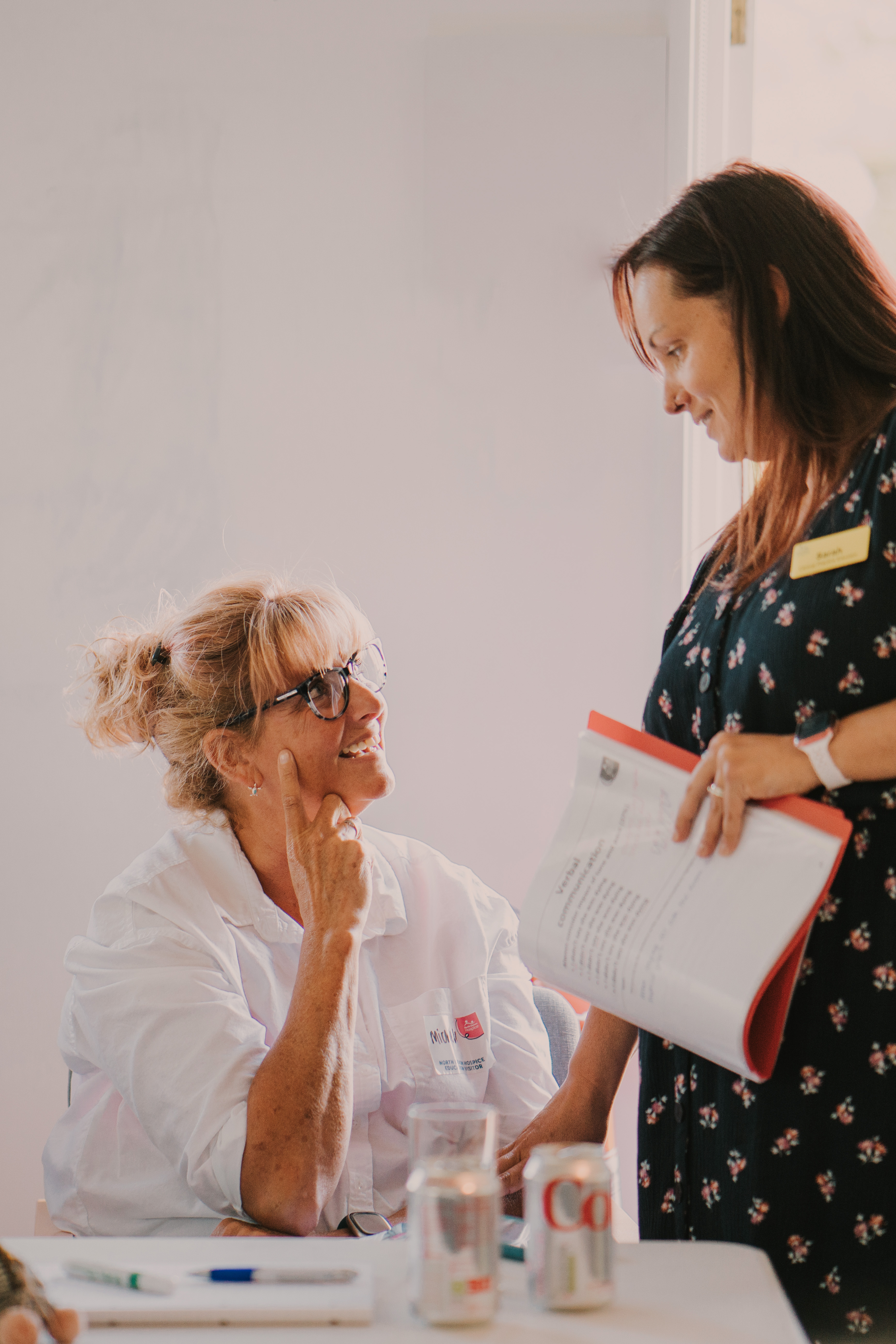 Two females, one standing, one seated, chatting at a training session