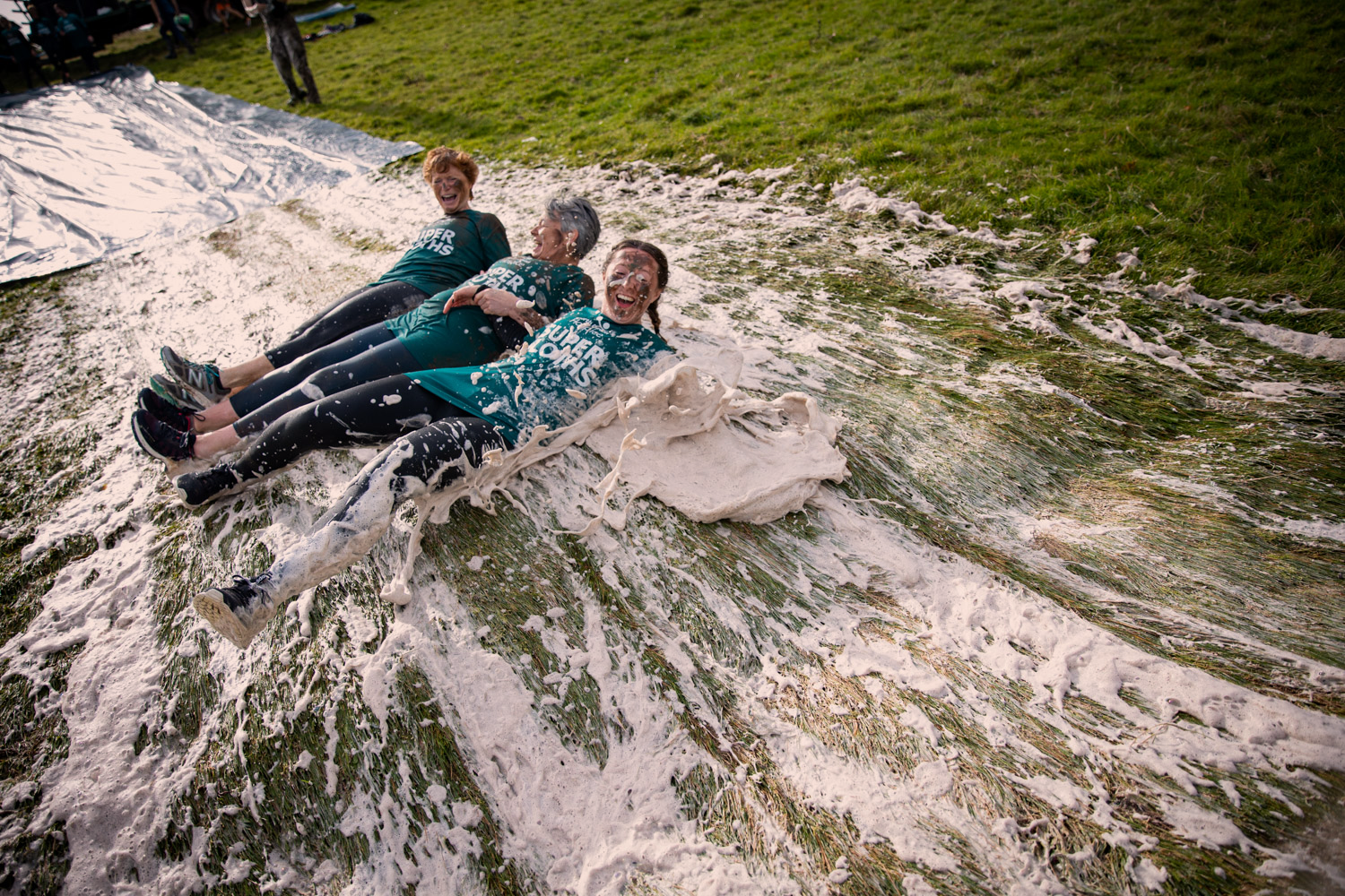 Three females, all wearing green tshirts, taking part in a commando style assault slide with water and soap