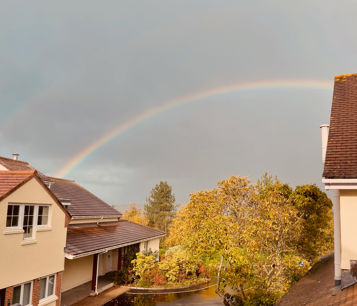 Outside of the hospice building showing trees, with grey skies and a rainbow visible