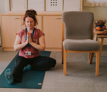 Female yoga instructor in a seated yoga pose on a green mat on the floor with her palms together