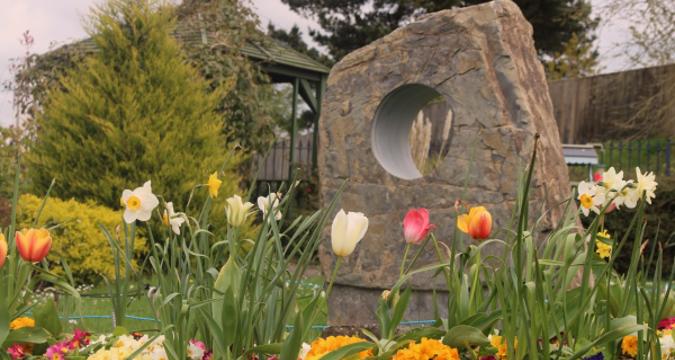 Large stone with hole in the centre, surrounded by colourful tulips, daffodils and other foliage in the garden