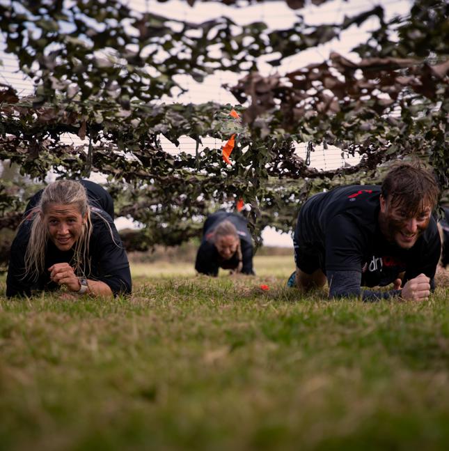 Female and male taking part in a commando style course, under netting crawling along the ground wearing face paint